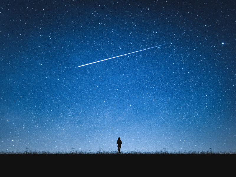 Silhouette eines Menschen vor dem Nachthimmel mit Sternschnuppe