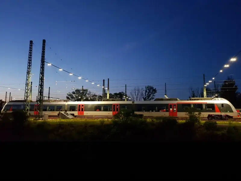 Ansicht einer beleuchteten Gleisanlage mit vorbeifahrendem Zug