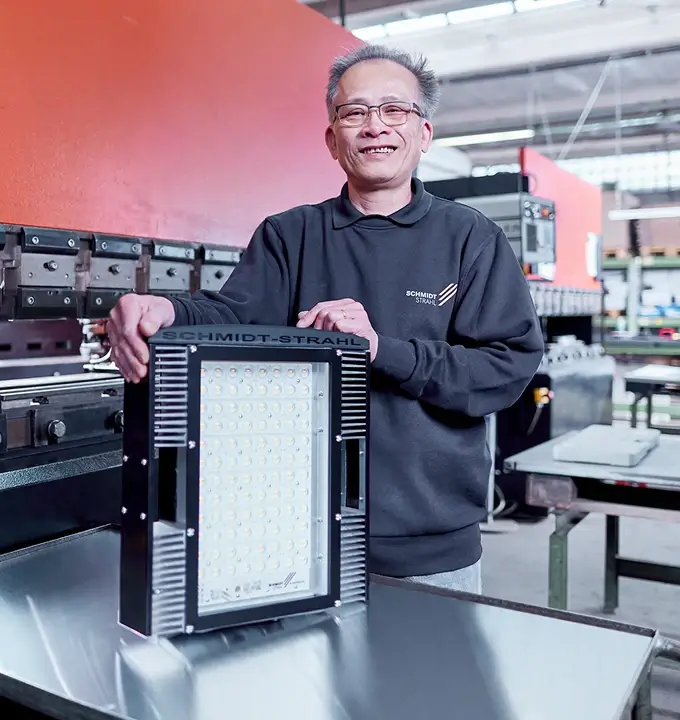 Mitarbeiter von Schmidt-Strahl präsentiert eine rechteckige LED-Industrieleuchte in der Fertigung.
