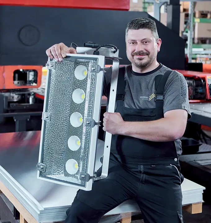 Mitarbeiter von Schmidt-Strahl hält eine robuste Flutlichtleuchte für Sport- und Außenanlagen.
