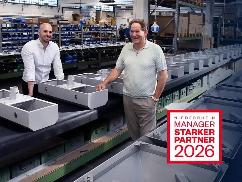 Geschäftsführer Jan-Marco Radermacher und Steffen Burckhardt in der Produktion zwischen gefertigten Leuchtengehäusen; eingeblendet ist die Auszeichnung „Niederrhein Manager – Starker Partner 2026“.